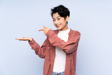 Young Asian girl over isolated blue background holding copyspace imaginary on the palm to insert an...