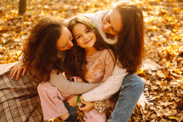 The homosexual family playing with her daughter in the autumn forest. The adventure is more fun when they are together. Autumn women.