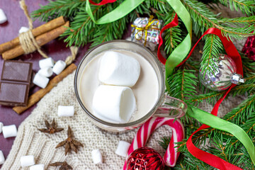 Top view of hot chocolate Christmas and New Year celebration cocoa drink in a glass cup with fir tree branches, holiday decorations and sweet red striped lollipops on wooden background.