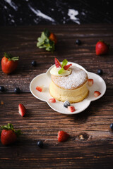 Fluffy souffle pancakes with cream and berries on white plate set on wooden table.