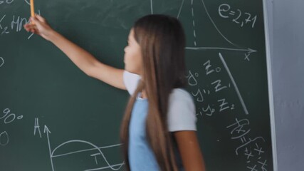 child holding pen while showing math formulas on chalkboard