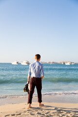 A dressed man walks along the sea after work.