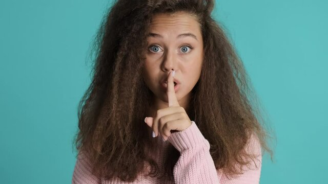 Beautiful brunette girl keep fore finger over lips showing keep secret safe expression isolated on blue background