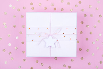 Top view of pastel pink gift box with bow and star with copy space on background decorated with golden confetti. Flat lay. Holiday festive concept.