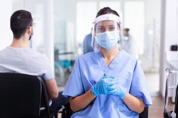 Nurse looking at camera wearing surgical face mask against coronavirus in hospital hallway as...