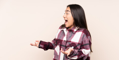 Naklejka premium Young Indian woman isolated on beige background with surprise expression while looking side