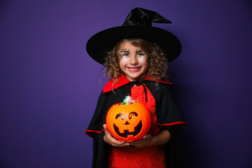 Cute little girl with pumpkin candy bucket wearing Halloween costume on purple background