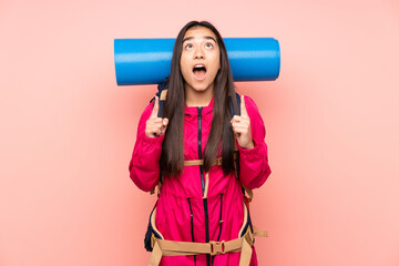 Young mountaineer Indian girl with a big backpack isolated on pink background pointing with the index finger a great idea