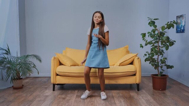 rack focus of kid in dress dancing near plants and sitting on sofa