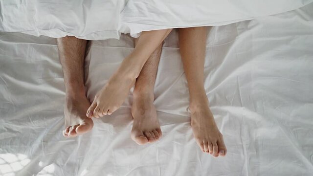 Couple in bed making love. male and female legs top view, white linens. sex