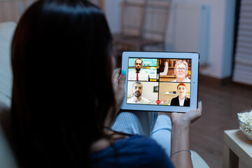 Fototapeta na wymiar Woman listening online training on tablet late at night sitting on sofa. Remote worker having virtual meeting consulting with colleagues on videocall and webcam chat using internet technology.