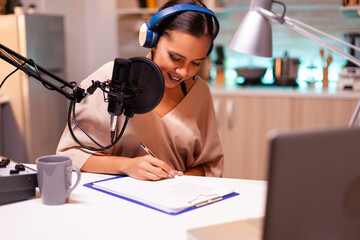 Influencer taking notes on clipboard while talking with followers during live on social media. Creative online show On-air production internet broadcast host streaming live content.
