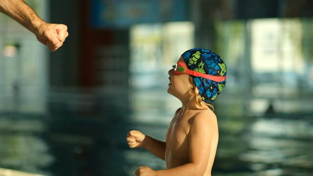 The concept of the success and interaction of the trainer with the little sportsman swimmer in the pool. A little boy athlete hits the coach with his fist.