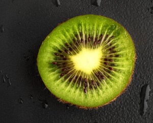 Half a juicy kiwi on a black background with water drops