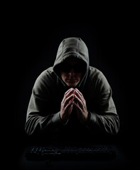 Dark hacker with hooded sweatshirt in front of keyboard in a black and low key setting