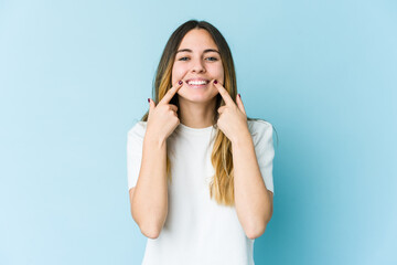 Fototapeta premium Young caucasian woman isolated on blue background smiles, pointing fingers at mouth.