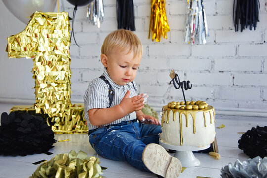 Boy blond 1 year on his birthday. Decorated photo zone with the first cake in black and gold. Crash cake.