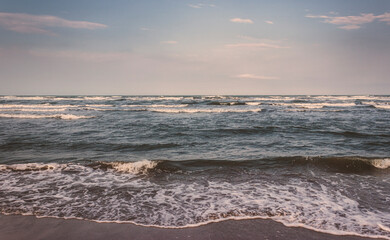 Fototapeta na wymiar On a cloudy day, sea waves roll over the sandy coast of the Adriatic Sea. Rimini. Italy