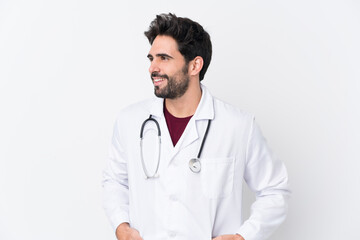 Fototapeta premium Young handsome man with beard over isolated white background wearing a doctor gown and with stethoscope
