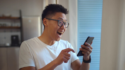 Handsome asian young man standing near window reading email on mobile phone 