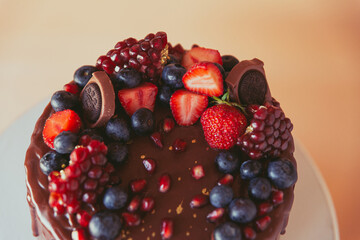 Appetizing chocolate cake decorated with strawberries, blueberries and a pomegranate on an orange background.