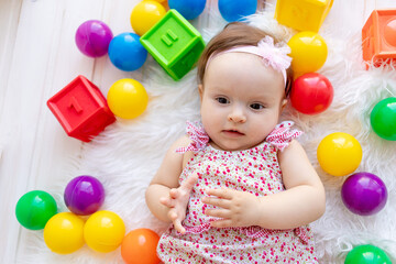 Fototapeta na wymiar a beautiful little baby girl is lying in red clothes on a white Mat among toys balls and cubes
