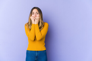 Young caucasian woman isolated on purple background biting fingernails, nervous and very anxious.