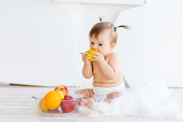 a little girl is sitting in a bright room with a plate of fruit and eating a pear