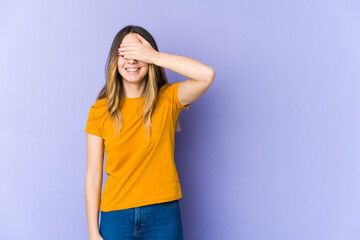 Young caucasian woman isolated on purple background covers eyes with hands, smiles broadly waiting for a surprise.