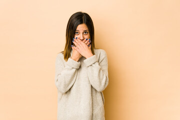 Young woman isolated on beige background covering mouth with hands looking worried.