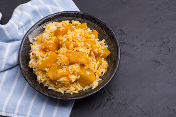 Rice with pumpkin curry in a black ceramic bowl, placed on a black table, top view.