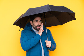 Man holding an umbrella over isolated yellow background whispering something