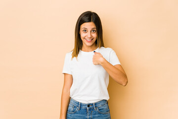 Young woman isolated on beige background surprised pointing with finger, smiling broadly.
