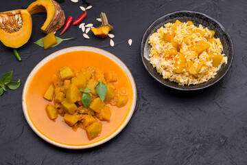 Curry or pumpkin soup with rice served in a ceramic platter on a black background - top view with writing space.