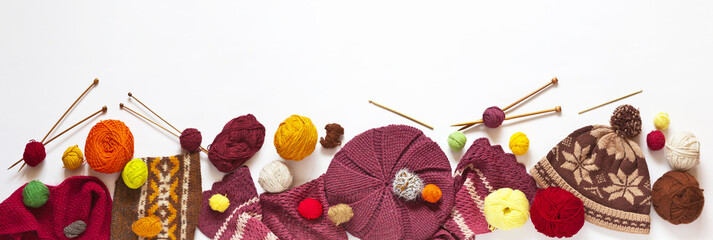 Panoramic top view on handmade knitted hats and scarves with balls of wool yarn on a white...