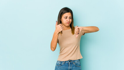 Young woman isolated on blue background showing thumbs up and thumbs down, difficult choose concept