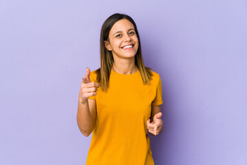 Young woman isolated on purple background pointing to front with fingers.