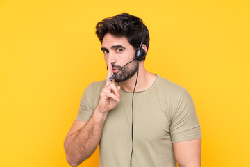 Telemarketer man working with a headset over isolated yellow background doing silence gesture