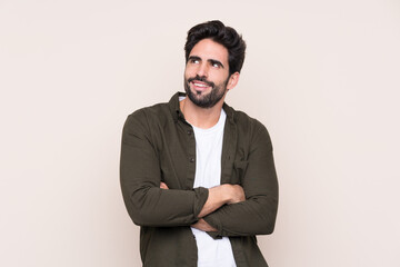 Young handsome man with beard over isolated background looking up while smiling