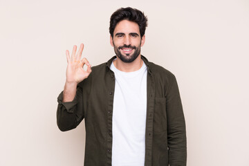 Young handsome man with beard over isolated background surprised and showing ok sign