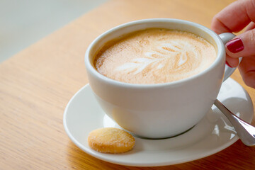 Cup of cappuccino coffee with biscuit on wooden table