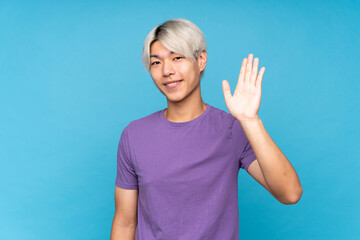 Fototapeta premium Young asian man over isolated blue background saluting with hand with happy expression