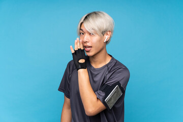 Young asian sport man over isolated blue background whispering something