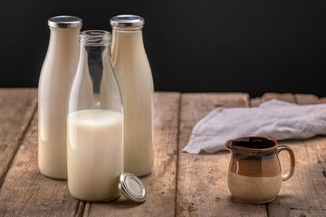 Bottles of fresh milk with small jug on rustic table
