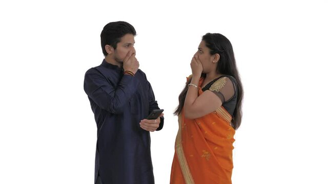 Indian couple looking at mobile screen. Finding something shocking and covering mouth with hand. Expressing bewilderment. Isolated on white background