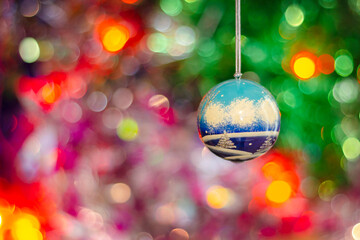 A Christmas tree toy ball on a background of multicolored tinsel and a glowing garland.