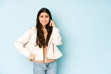 Young indian woman on blue background covering ears with hands.