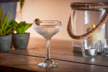 Cocktail in martini glass with olive on a table with potted plants and candles