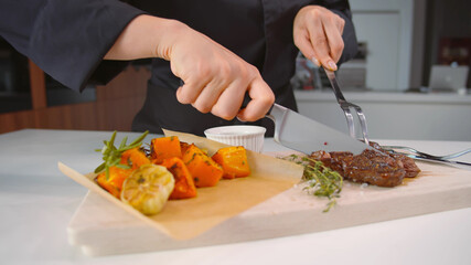 Close up of chef cutting beef steak served with baked spiced pumpkin on