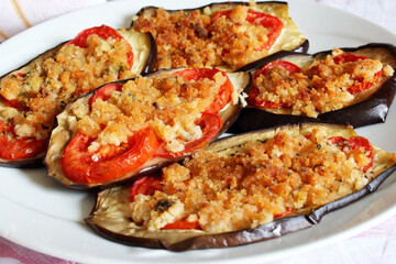 Melanzane e pomodori tagliati a fette  gratinate nel forno e disposte su un piatto bianco.